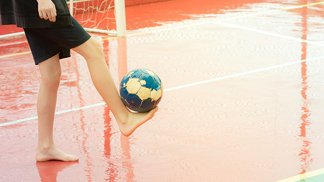 一个赤脚的男孩在潮湿的操场上踢足球